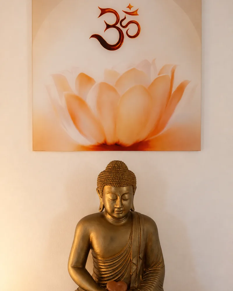 Wandbild mit Lotusblüte und Om-Zeichen über einer goldenen Buddha-Figur im Praxisraum